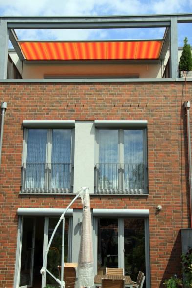 Markise orange-gelb-gestreift auf Dachterrasse und hellgrauen Fenstern